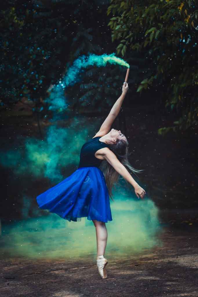 Photo of a modern dancer holding a stick producing blue smoke in the forest