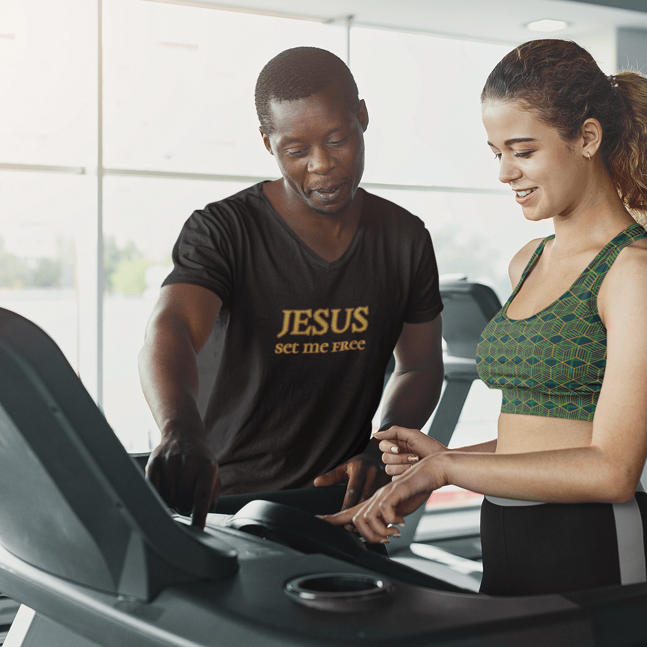 Man wearing “Jesus Set Me Free” Short Sleeve V-Neck T-Shirt by Fitness for Worship and woman wearing Green Geometric Sports Bra by FItness for Worship in a gym