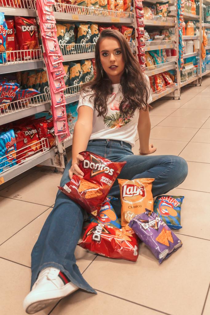 A woman sitting on the floor of a grocery store, surrounded by packaged chips